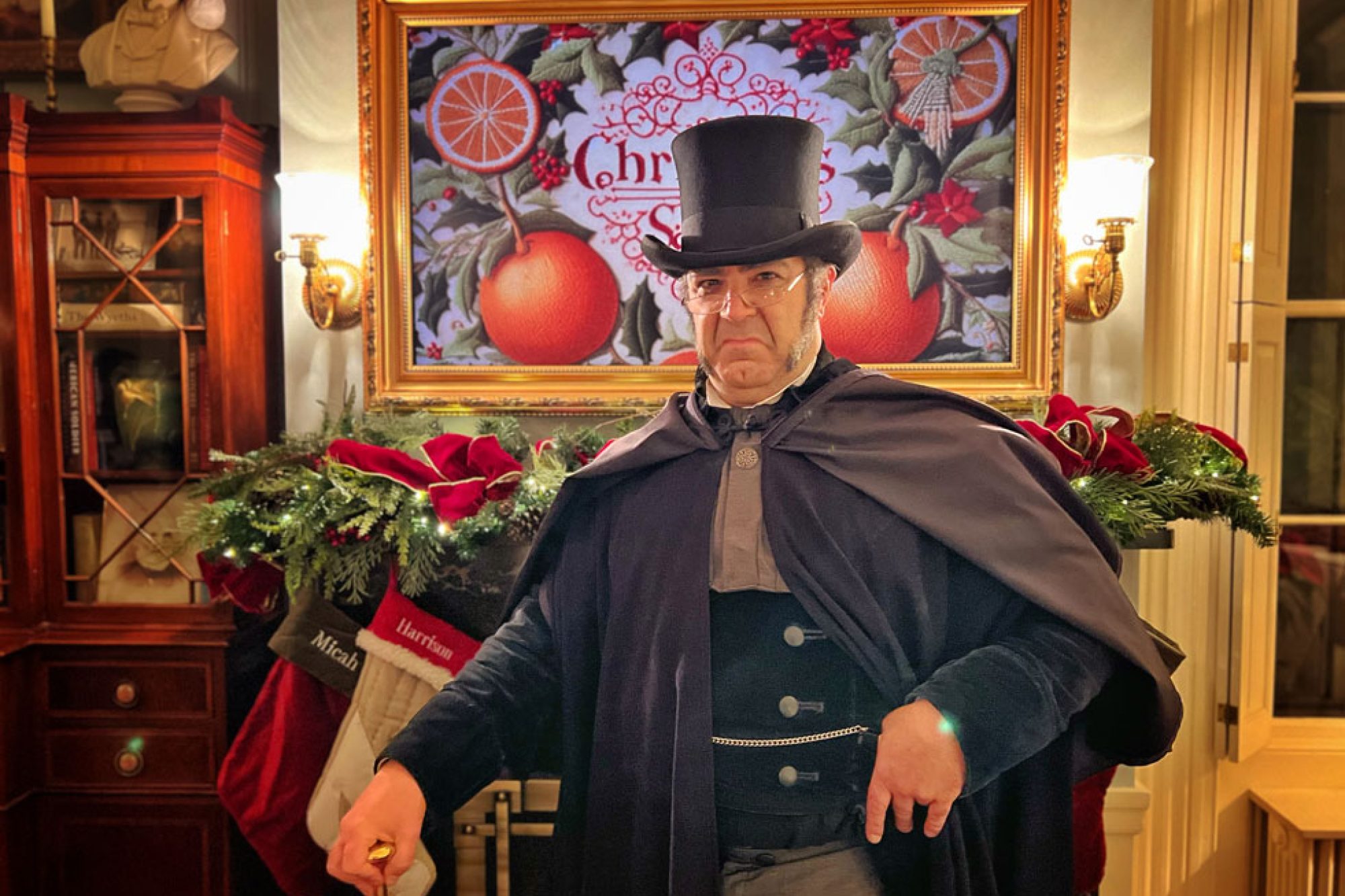 A man dressed as Charles Dickens standing in front of a fireplace